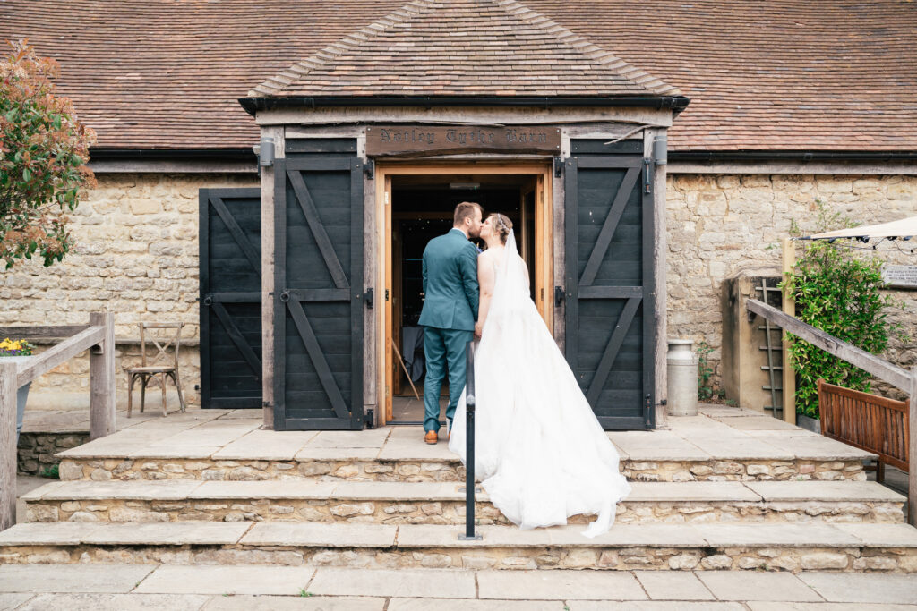 Bridge and groom on the steps outside Notley Tythe Barn, groom in green suit, and bride in white dress